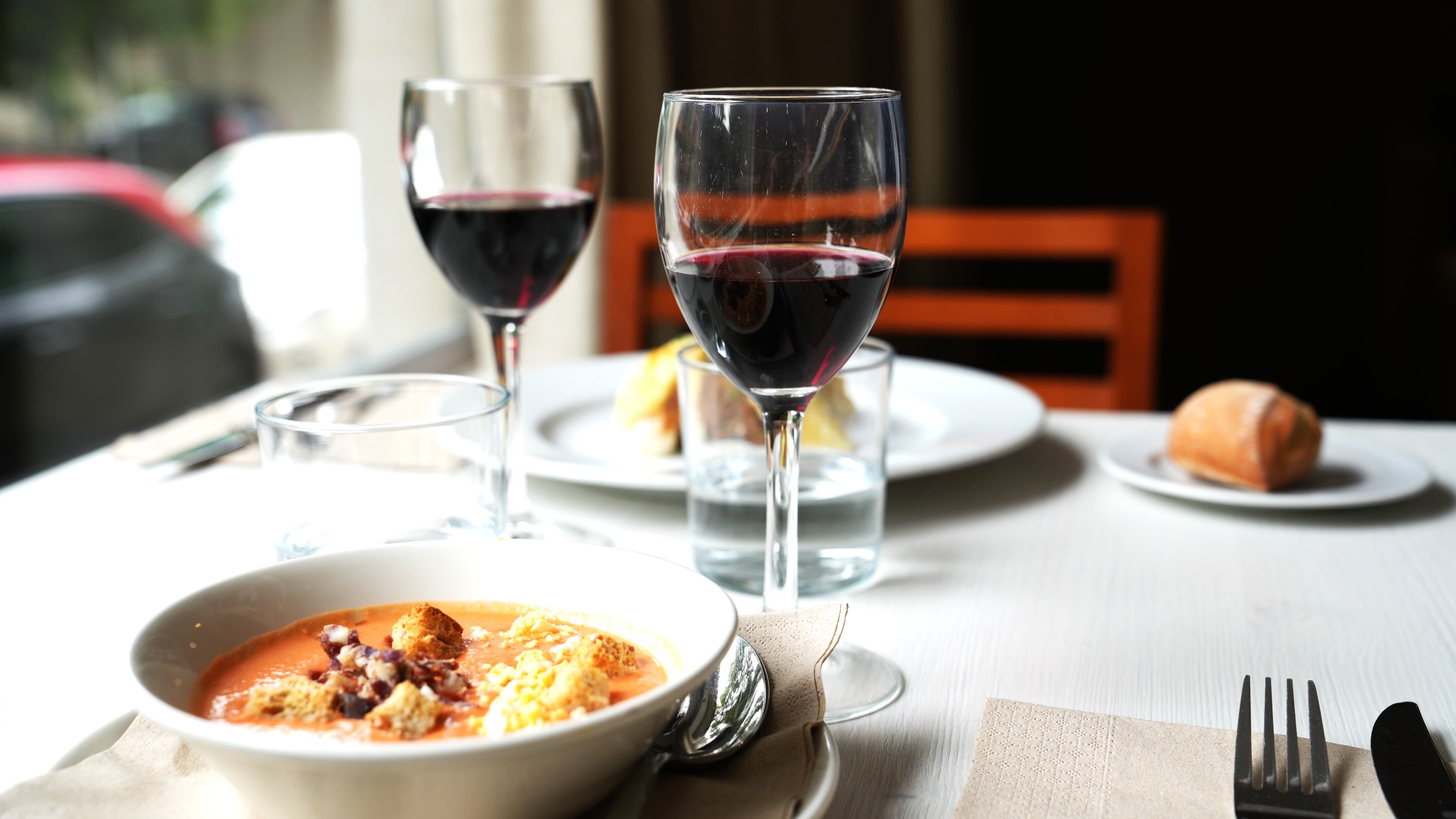 a bowl of soup sits on a table next to two glasses of red wine