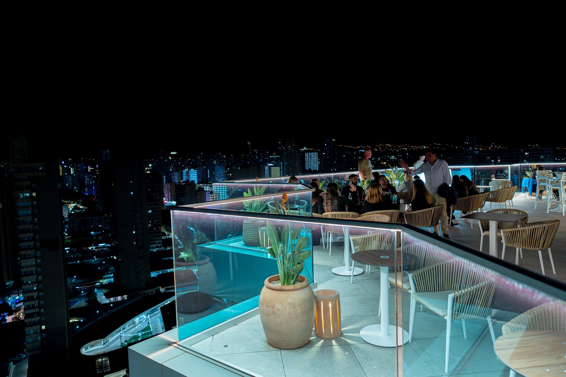 a group of people sitting at tables on a balcony overlooking a city