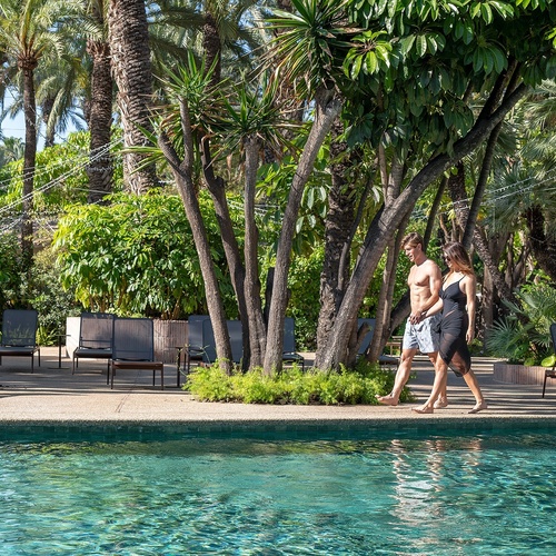 a man and a woman are walking by a pool surrounded by palm trees