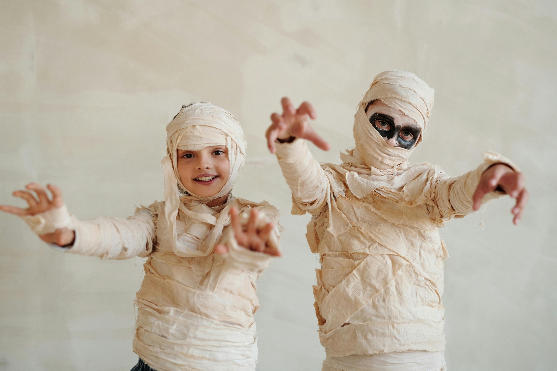 two children dressed in mummy costumes with their arms outstretched