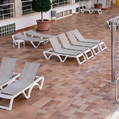 Cadeiras de Port Hotels: Corporativa elegantes e vazias em um terraço com azulejos de terracota e uma piscina.
