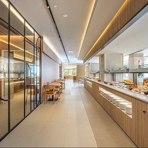 Buffet en hotel moderno con mesas de madera y platos apilados. Port Hotels: Corporativa