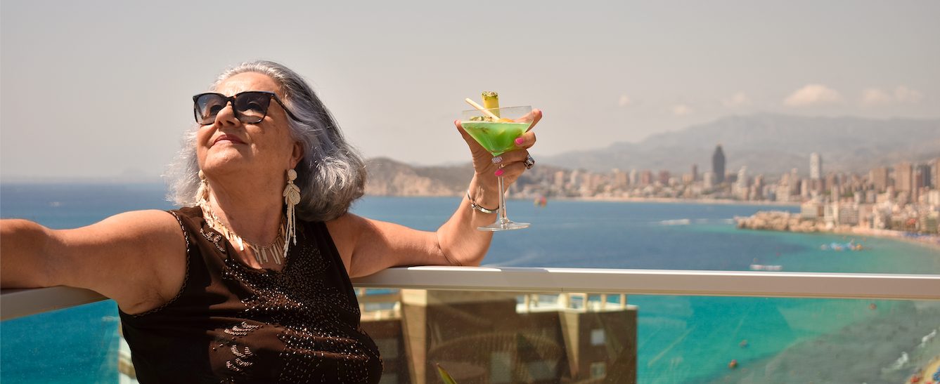 a woman is holding a martini in front of the ocean