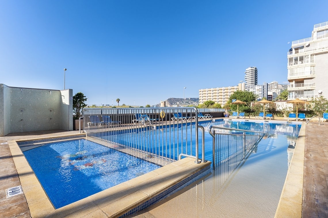 a swimming pool with blue chairs and a mountain in the background