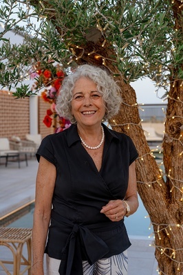 a woman wearing a black shirt and pearls smiles in front of a tree - 