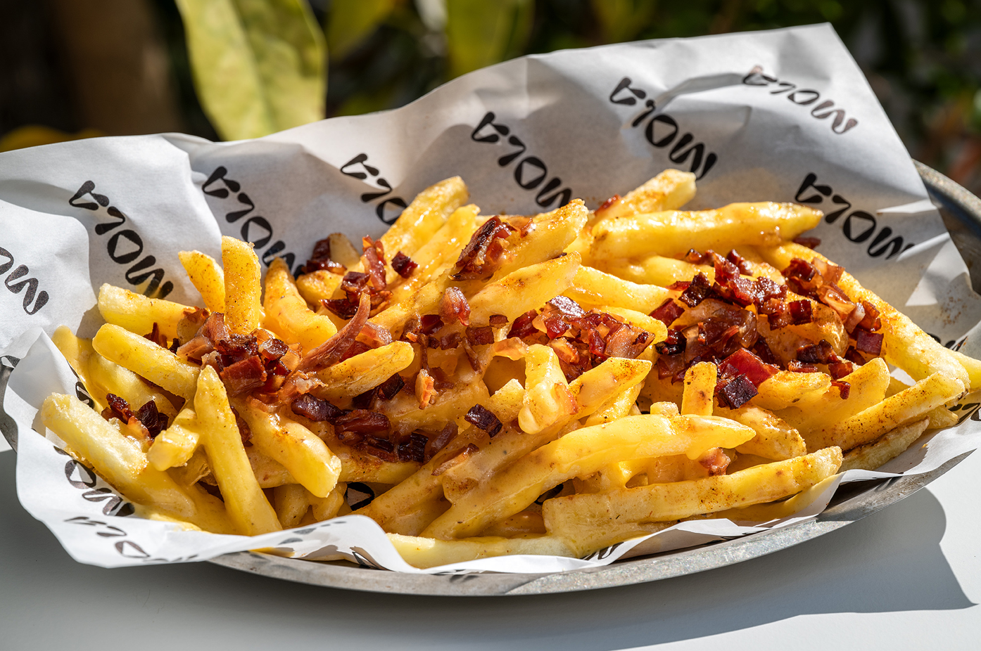 a plate of french fries with bacon on a paper that says mola