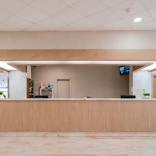 Mostrador de recepción de hotel moderno con detalles de madera clara y mármol, acentuado por una iluminación integrada y un ambiente pulcro.