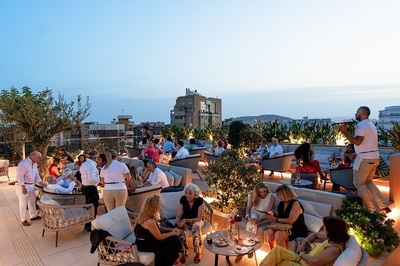 un hombre lleva una bandeja de bebidas a un grupo de personas sentadas en una terraza - 