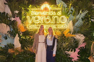 two women standing in front of a sign that says bienvenido al verano - 