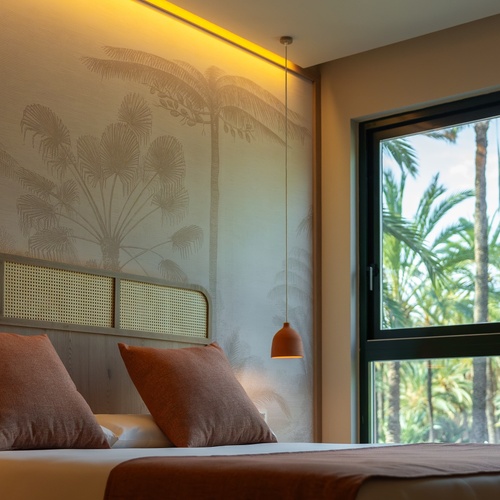 una habitación con una cama y una ventana con palmeras en el fondo