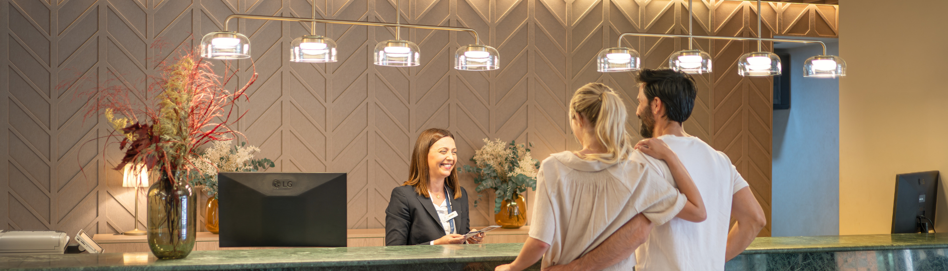 Recepción de hotel. Recepcionista sonriente da la bienvenida a una pareja.