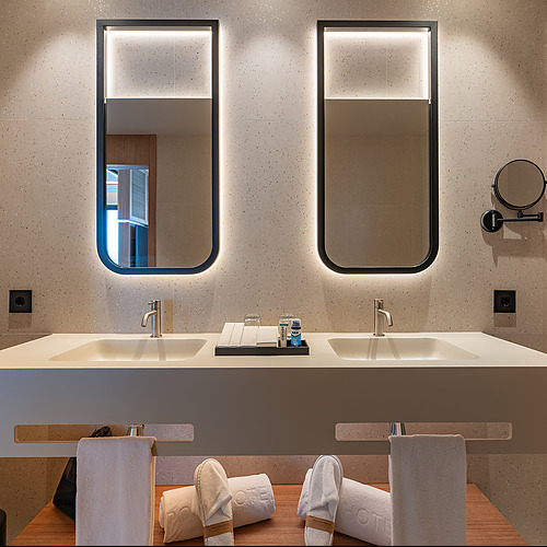Baño de hotel moderno con doble lavabo, espejos iluminados y Port Hotels: Corporativa de lujo.