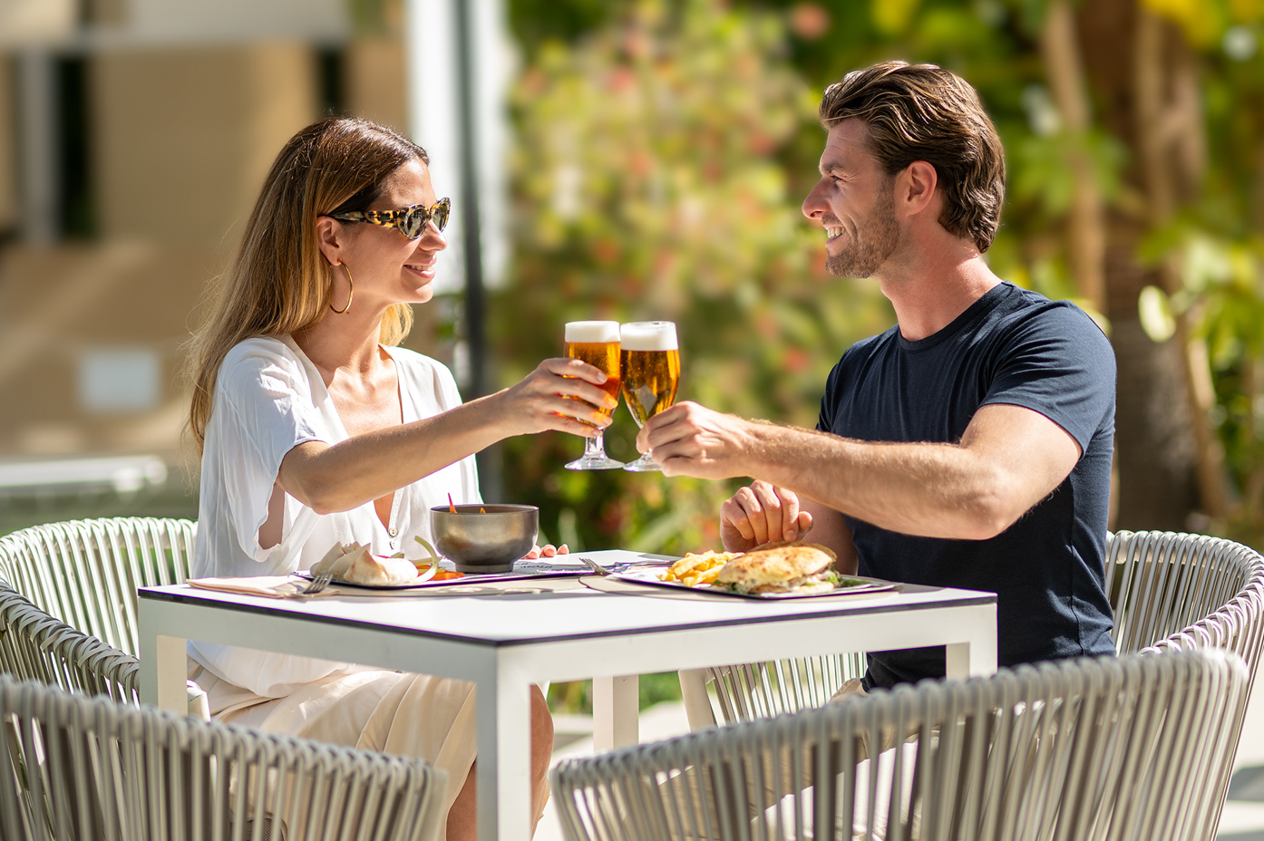 un hombre y una mujer brindan con cervezas en una mesa al aire libre