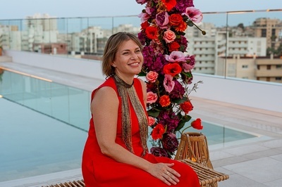 una mujer con un vestido rojo está sentada en un banco frente a un ramo de flores - 