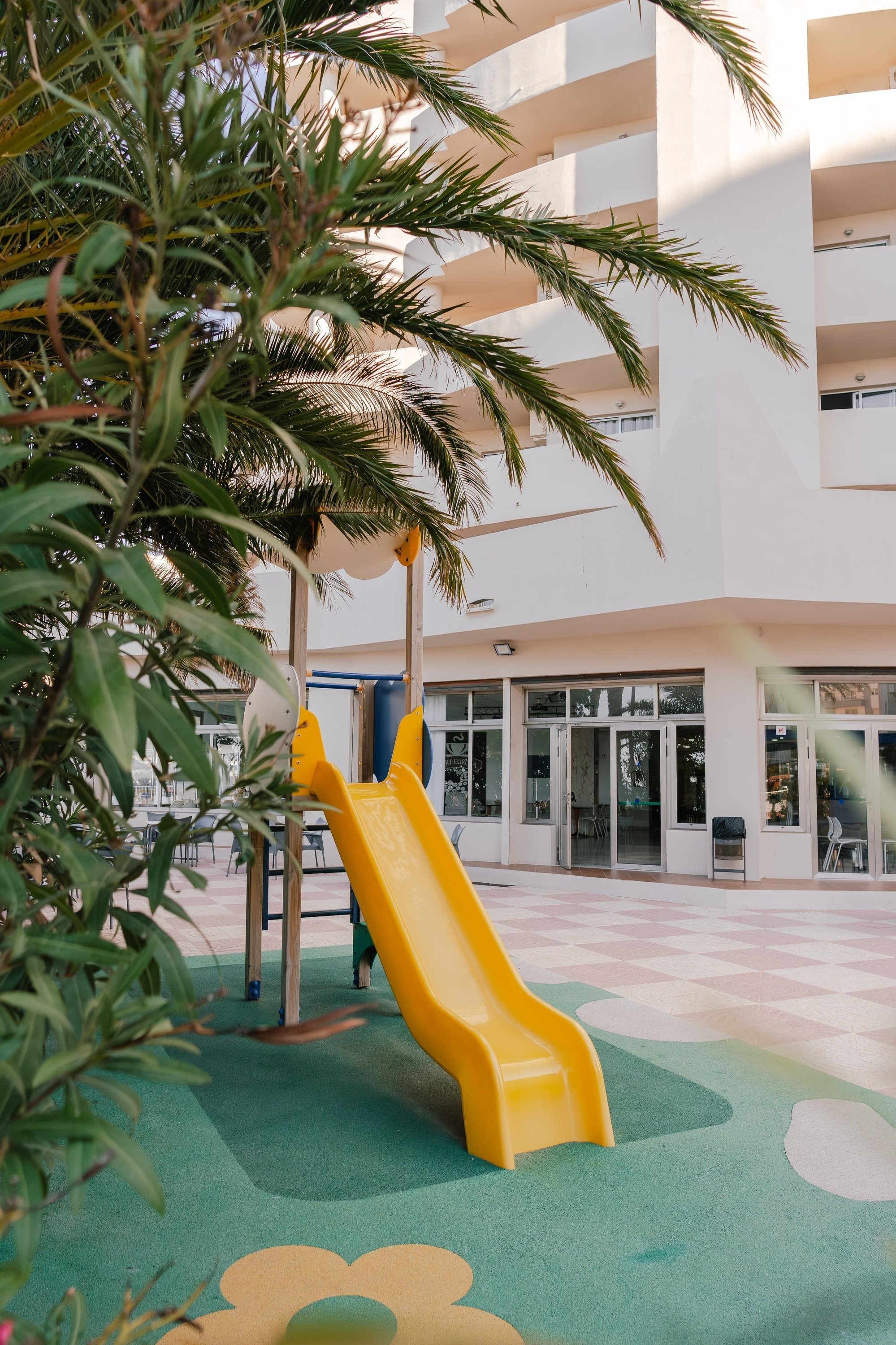 un tobogán amarillo en un patio con una palmera en el fondo