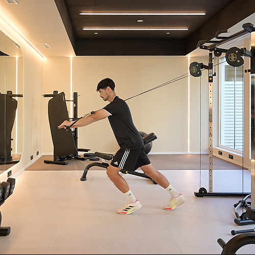 Hombre entrenando con máquina de cables en gimnasio de hotel con espejos y luces LED. Port Hotels: Corporativa