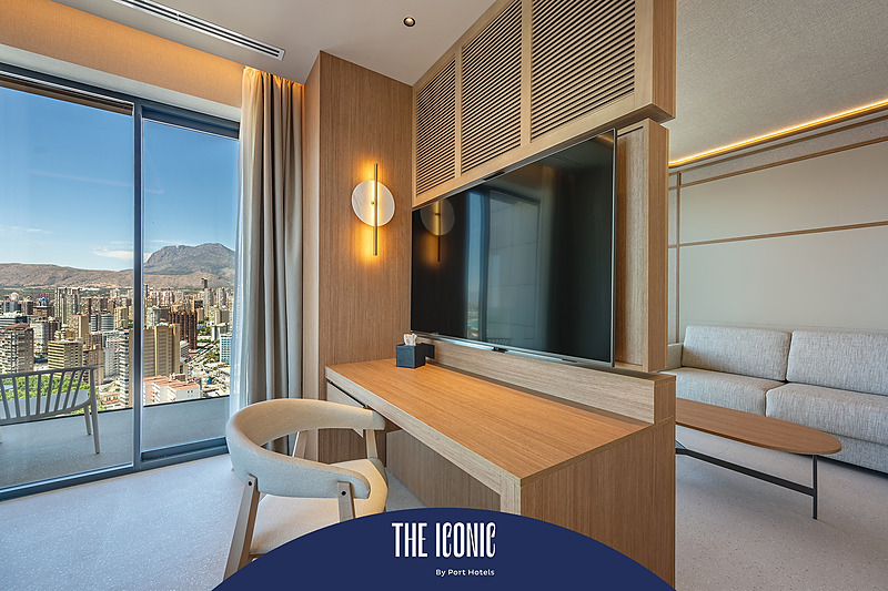 Elegante habitación de hotel con vista panorámica, escritorio de madera, sofá y TV. La estadía perfecta en Port Hotels: Corporativa.