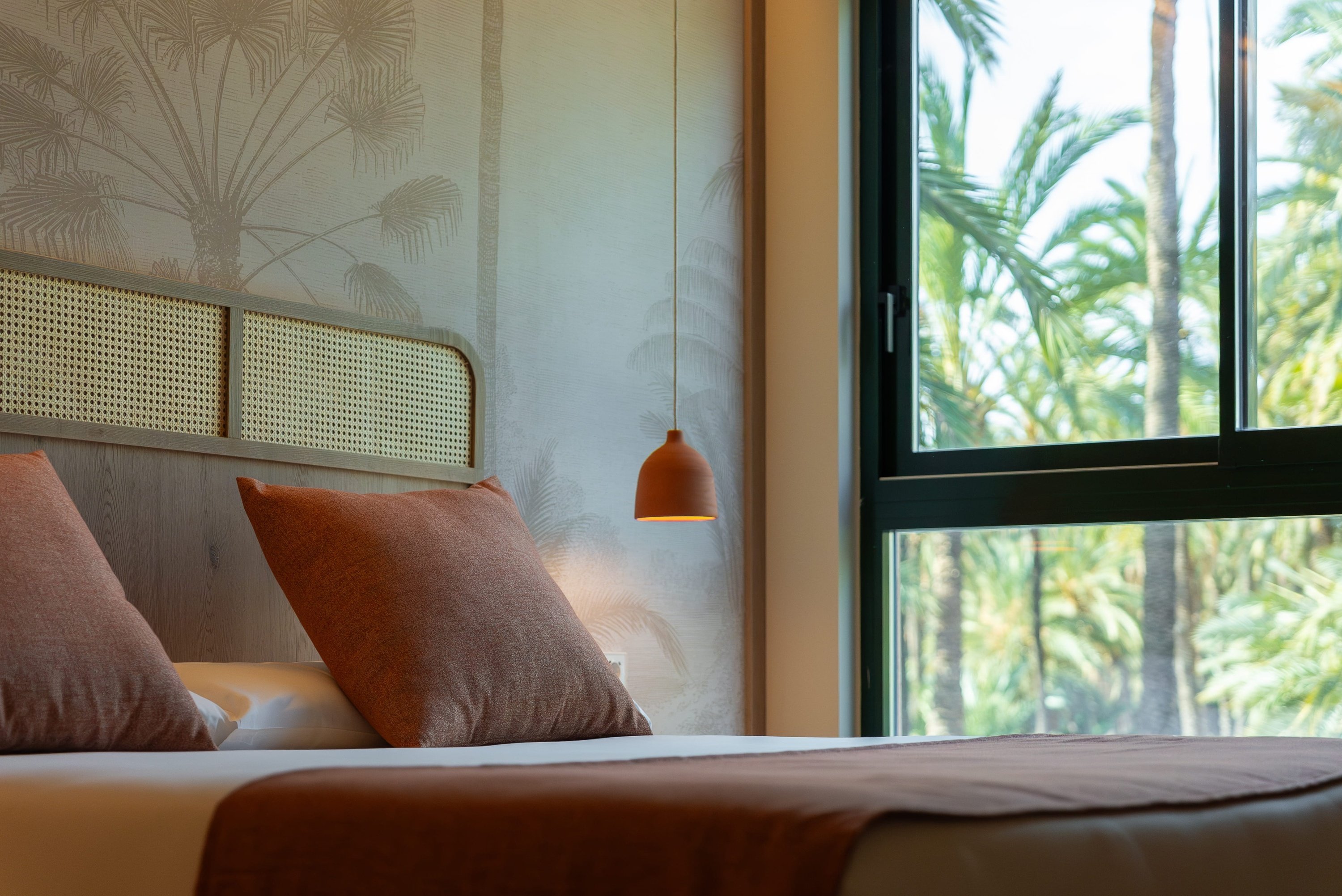 a bedroom with a bed and a window with palm trees in the background