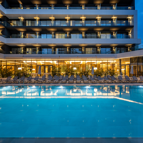 una piscina al frente de un hotel con sillas y mesas alrededor