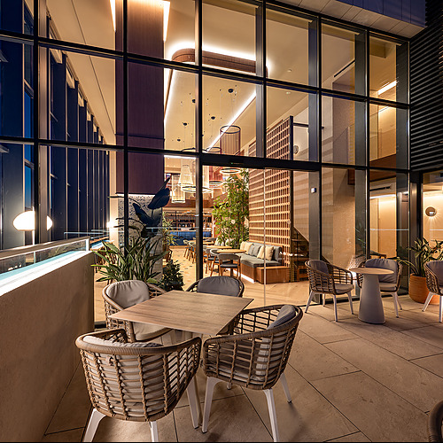 Terraza de hotel con mesas y sillas de ratán, vista urbana nocturna, perfecta para cenar al aire libre o tomar algo. Ideal para tu próxima Port Hotels: Corporativa.