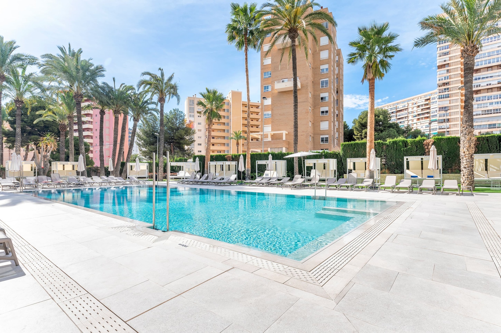 una gran piscina rodeada de palmeras y sillas con un edificio en el fondo