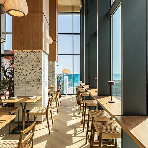 Interior de hotel moderno con vistas al mar, mesas y sillas de madera, ideal para disfrutar dePort Hotels: Corporativa.