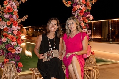 two women sit next to each other in front of flowers - 