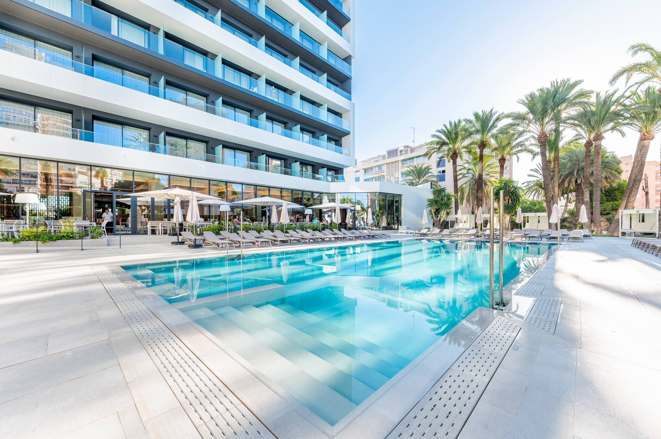 una gran piscina rodeada de palmeras frente a un gran edificio