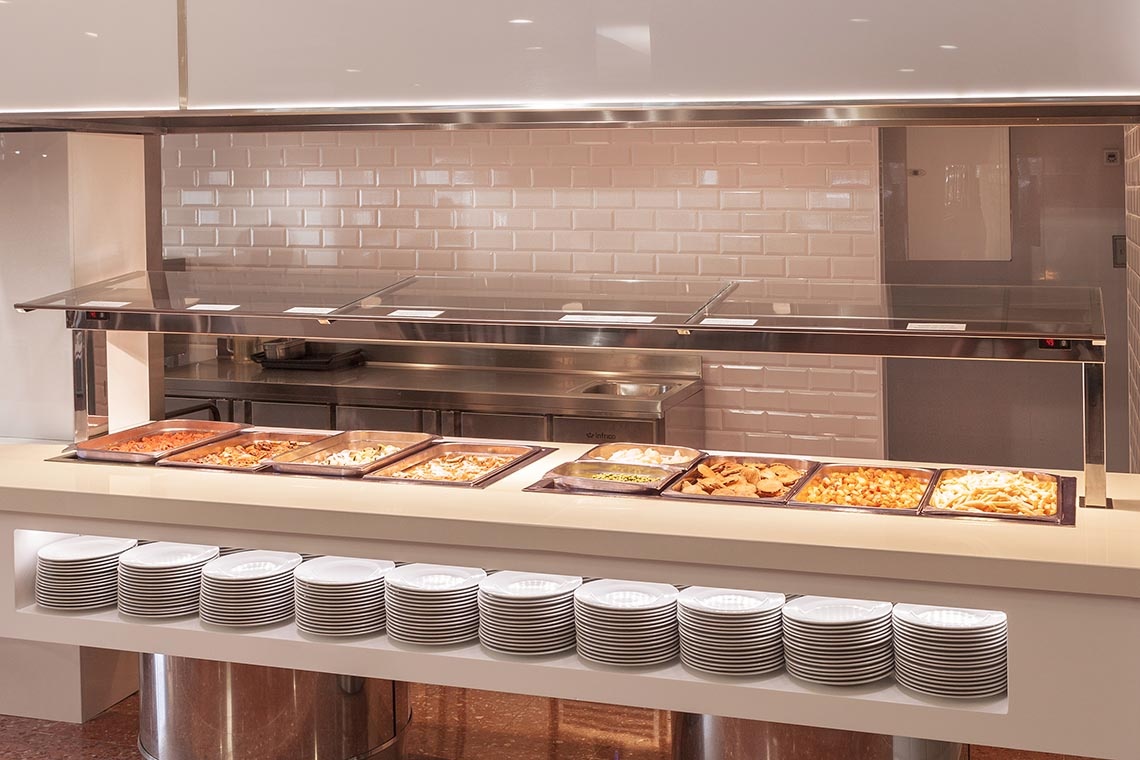Buffet do Port Hotels: Corporativa com pratos variados e pilhas de pratos brancos.