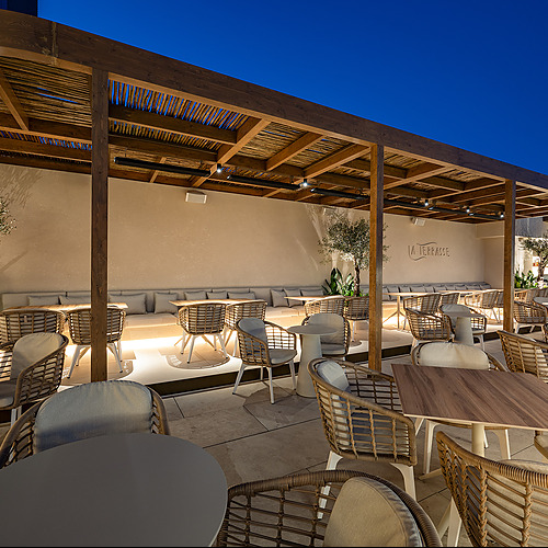 Terraza de hotel con mesas y sillas de ratán, ideal para disfrutar dePort Hotels: Corporativa al atardecer.