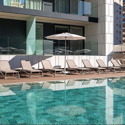 Sillas de piscina junto a la piscina turquesa, área de descanso, cabañas y arquitectura moderna. Port Hotels: Corporativa