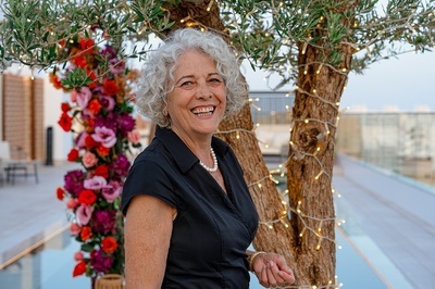 a woman in a black shirt and pearls smiles in front of a tree - 