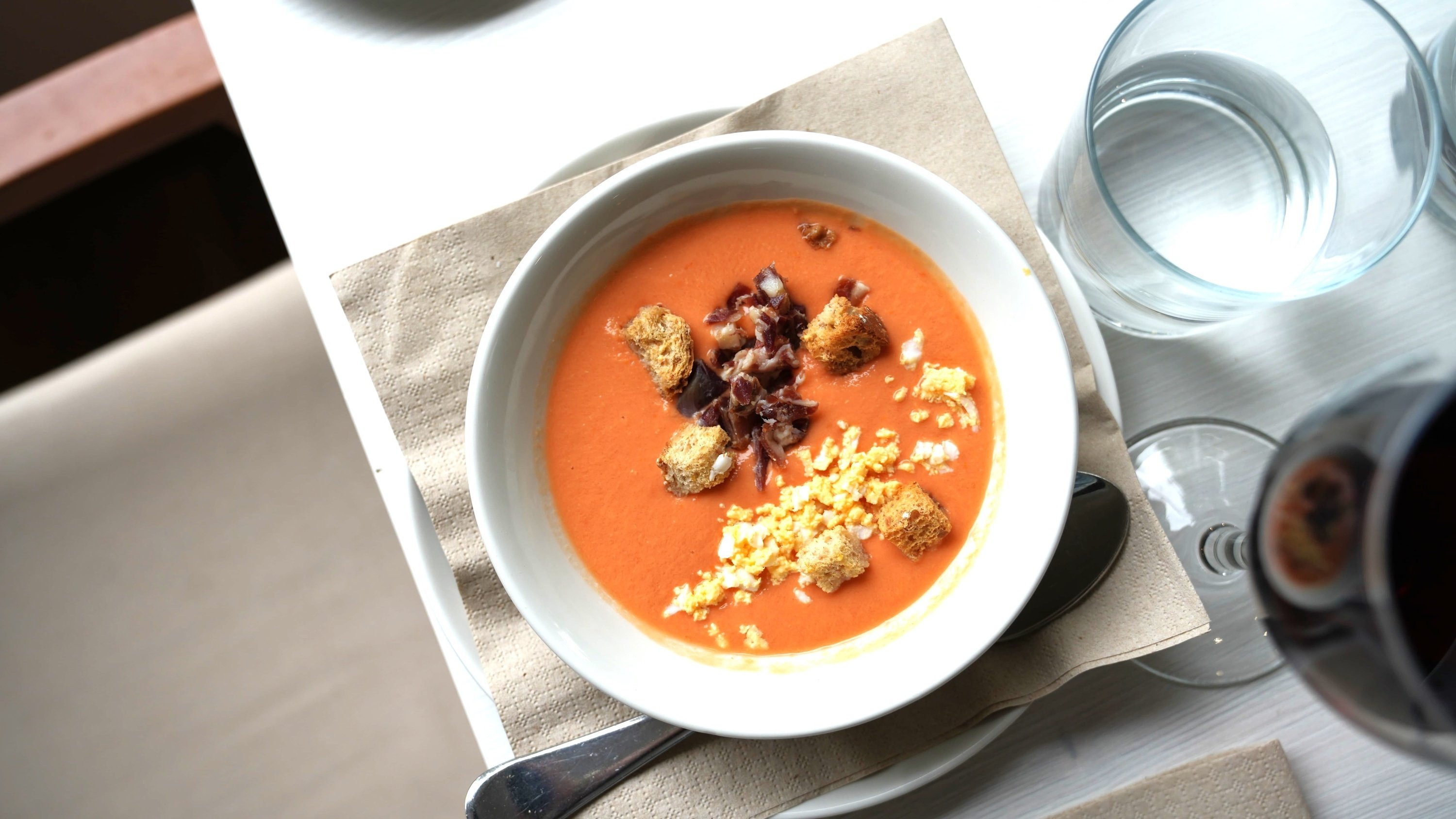 un tazón de sopa de tomate con croutons y jamón encima