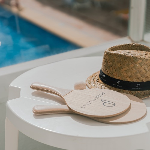 a straw hat sits on a white table next to a pair of rackets that say porthotel