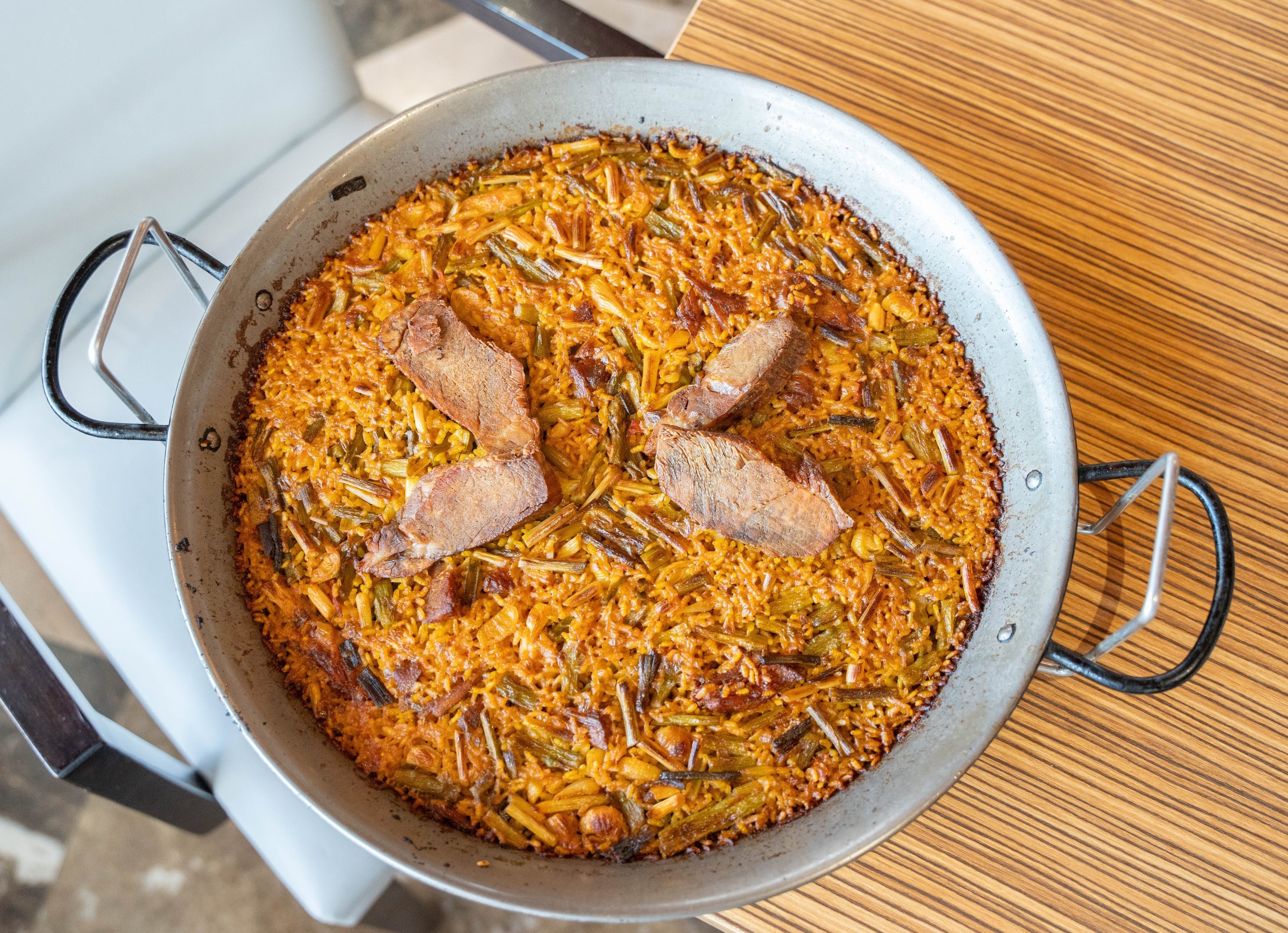 Authentic paella with saffron rice, green vegetables, and meat in a large pan, offered at our hotel.