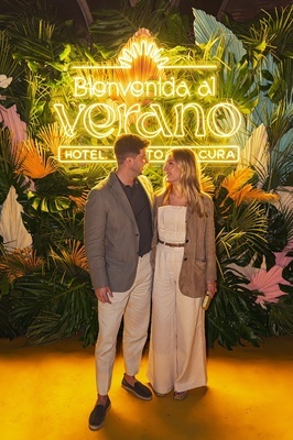 a man and woman standing in front of a sign that says bienvenido al verano - 