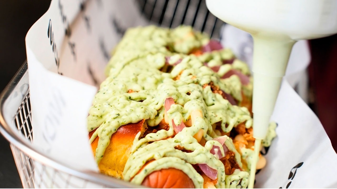 a hot dog with avocado sauce being poured on it