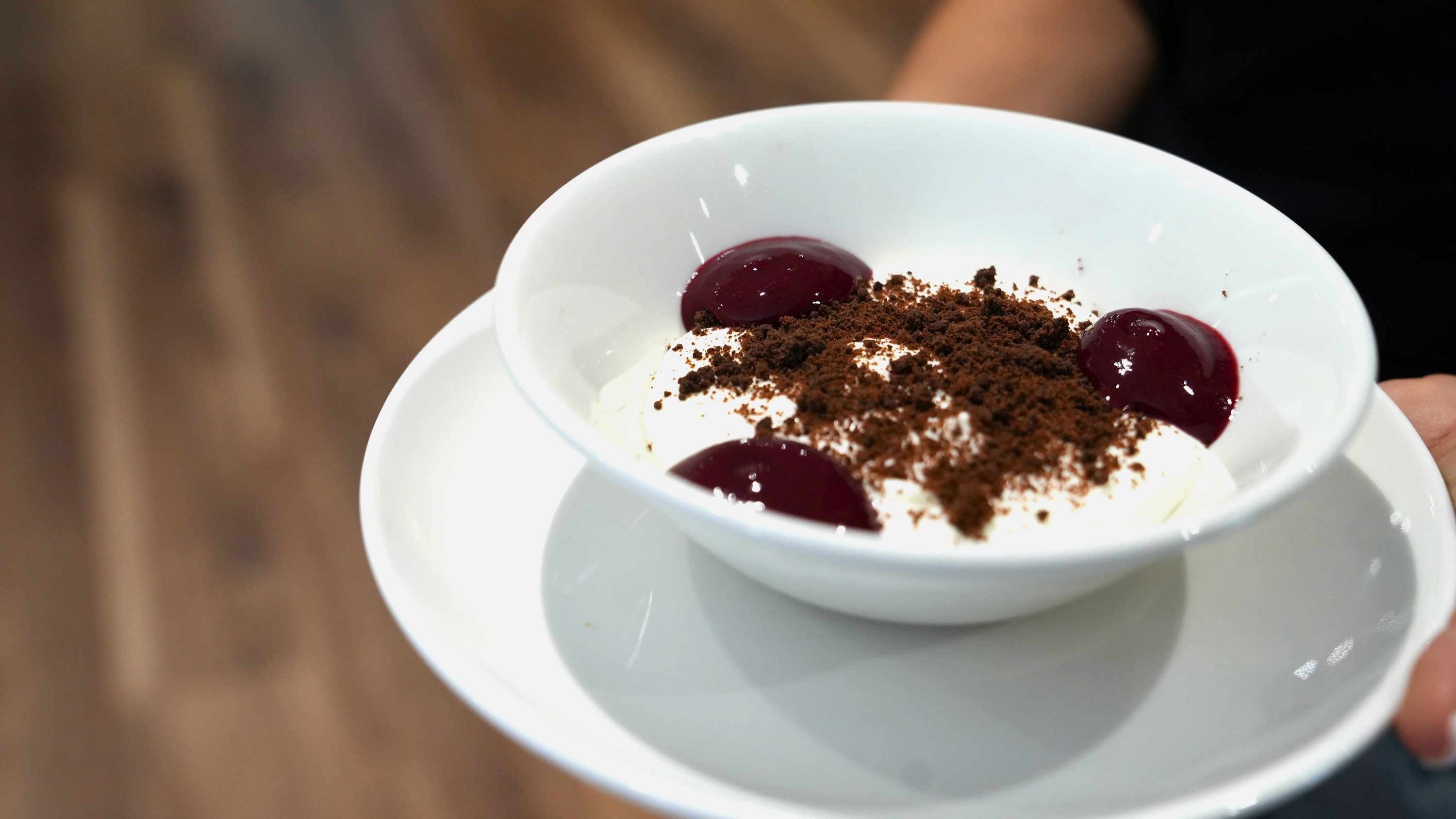 una persona sostiene un plato blanco con un postre y cerezas encima