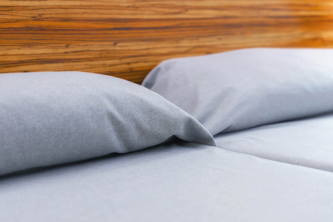 una cama con sábanas grises y una cabecera de madera