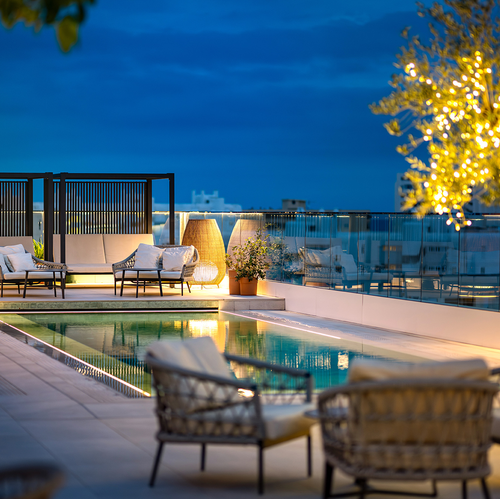 una piscina rodeada de muebles y un árbol con luces amarillas