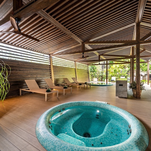 a hot tub is surrounded by lounge chairs under a wooden roof