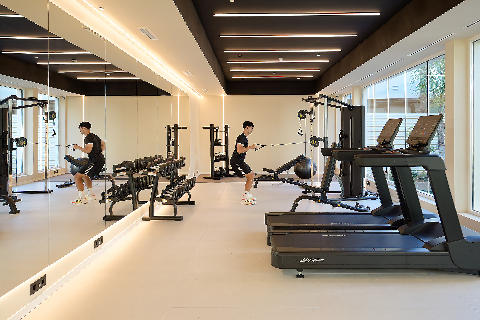 Gimnasio moderno con un hombre entrenando en máquina de cables y cintas de correr. Bienestar Port Benidorm Hotel & Spa | Port Hotels | Web Oficial