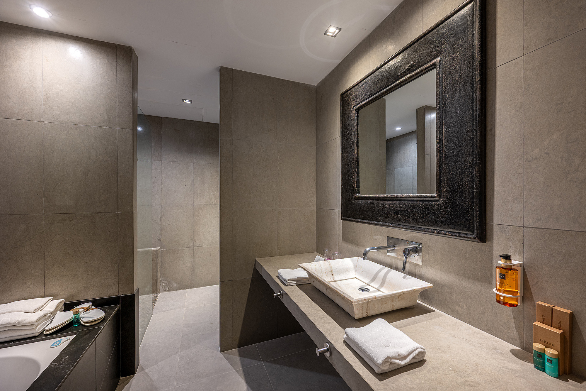Baño moderno de hotel con lavabo de piedra, espejo y amenities. Ubicación ideal para Port Hotels: Huerto del Cura.