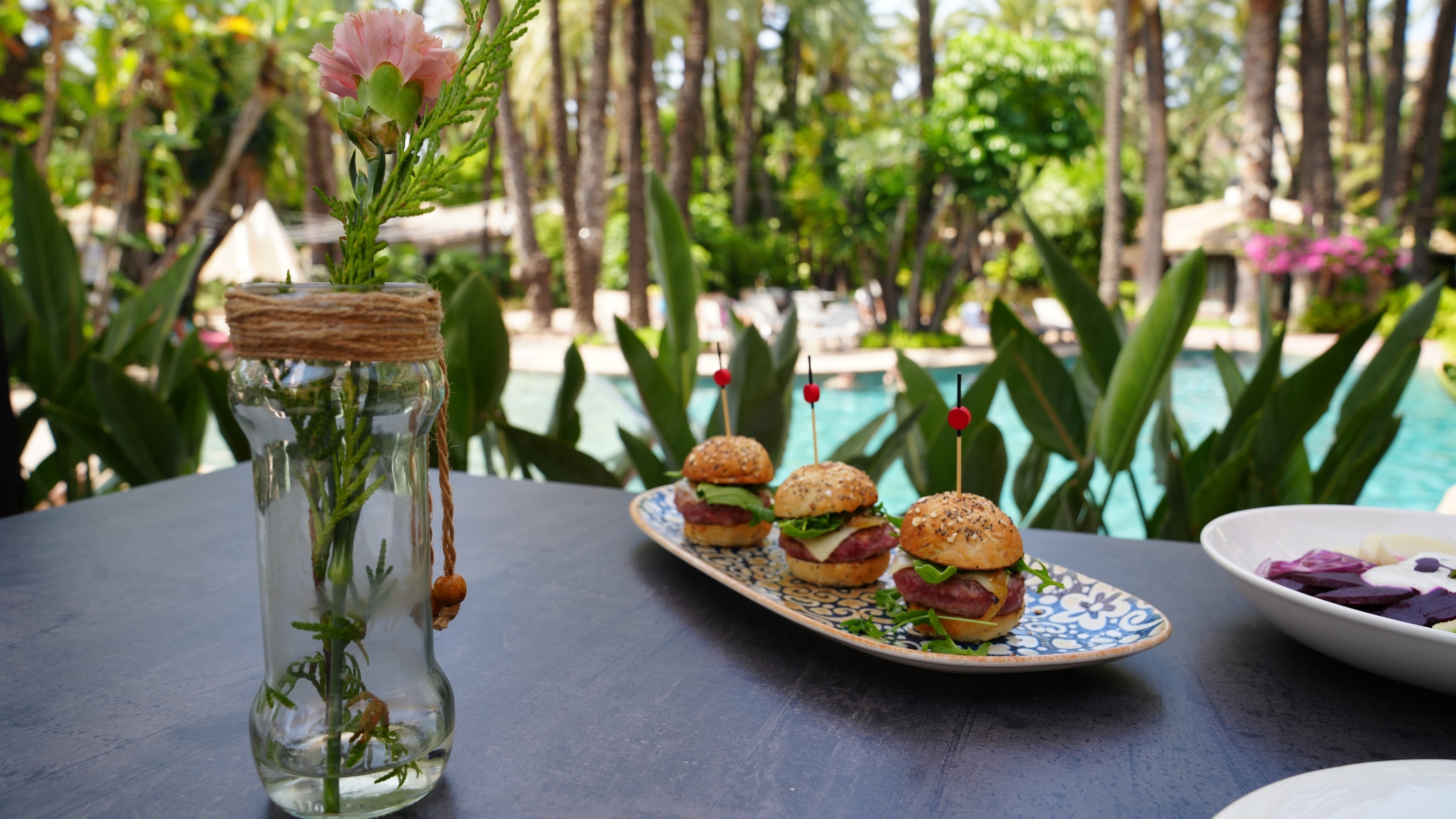 un jarrón de flores junto a un plato de hamburguesas