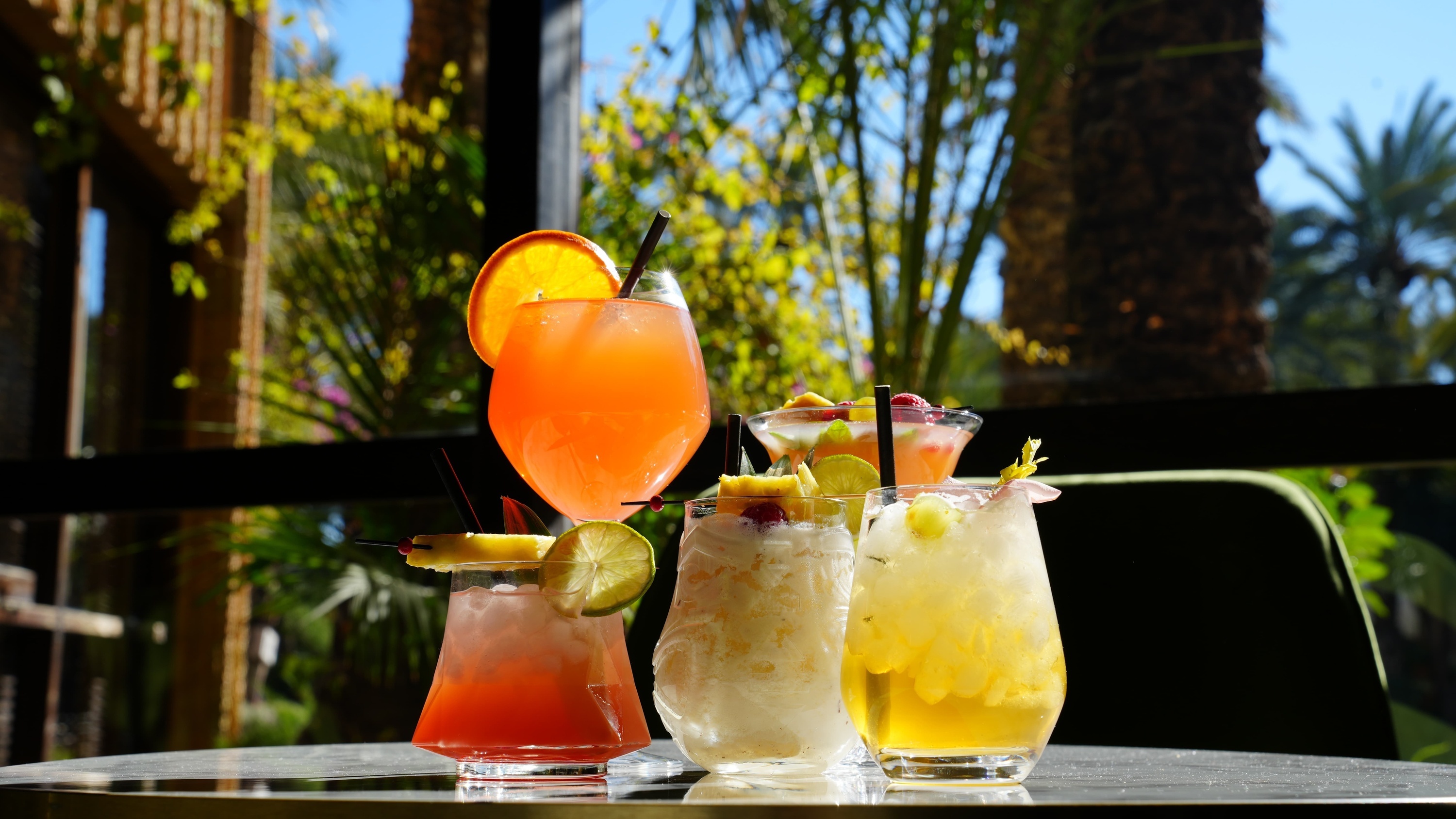 three drinks are on a table with a palm tree in the background