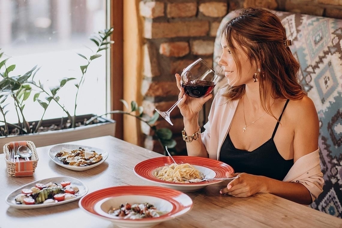 a woman sitting at a table with plates of food and a glass of wine