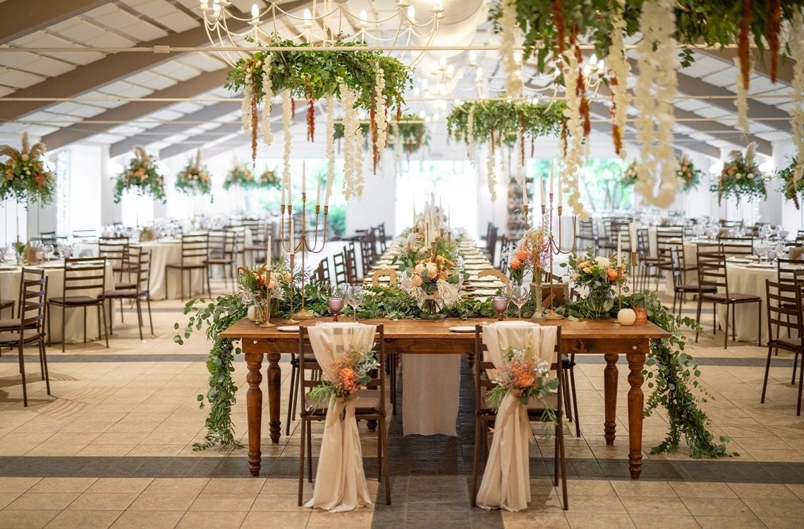 a long table in a large room with flowers hanging from the ceiling