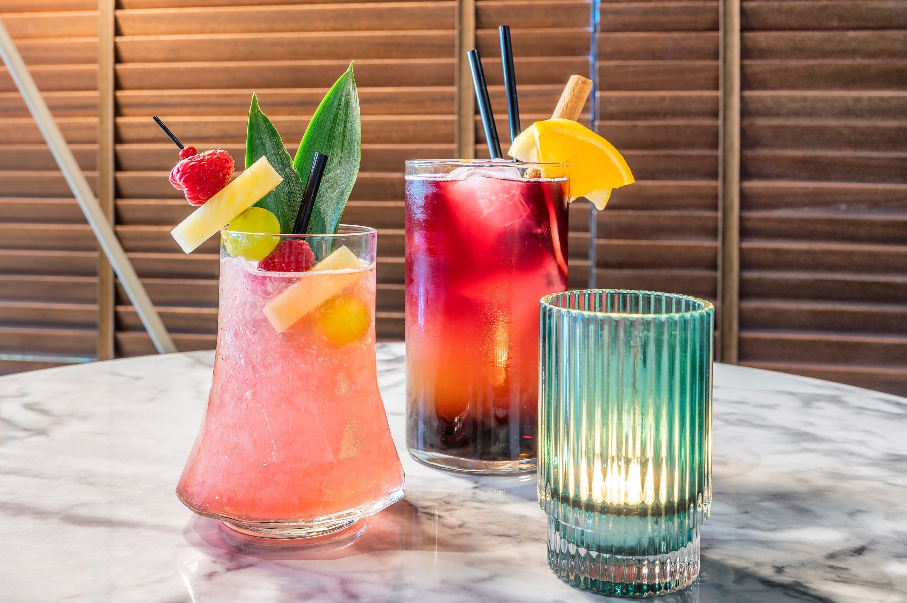 three different colored drinks are on a table with a candle