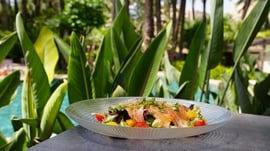 un plato de ensalada con pescado y verduras está sobre una mesa frente a una piscina