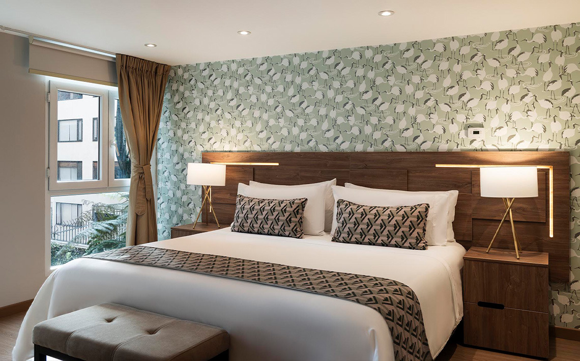 Elegante habitación de hotel con cama extragrande (king), papel pintado de diseño y lámparas de mesita de noche.